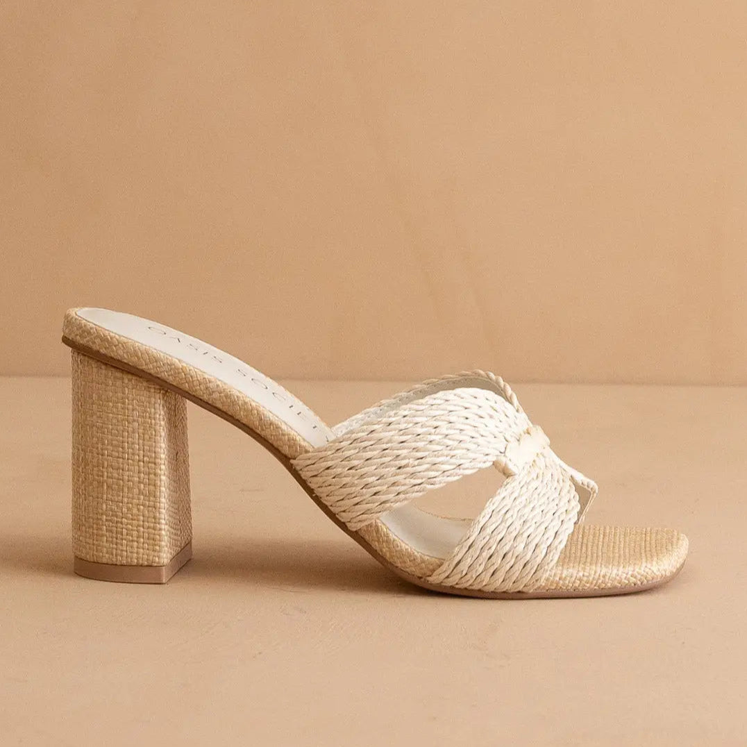 An off white raffia heel with a crisscross strap and a 3-inch heel, set against a neutral background.