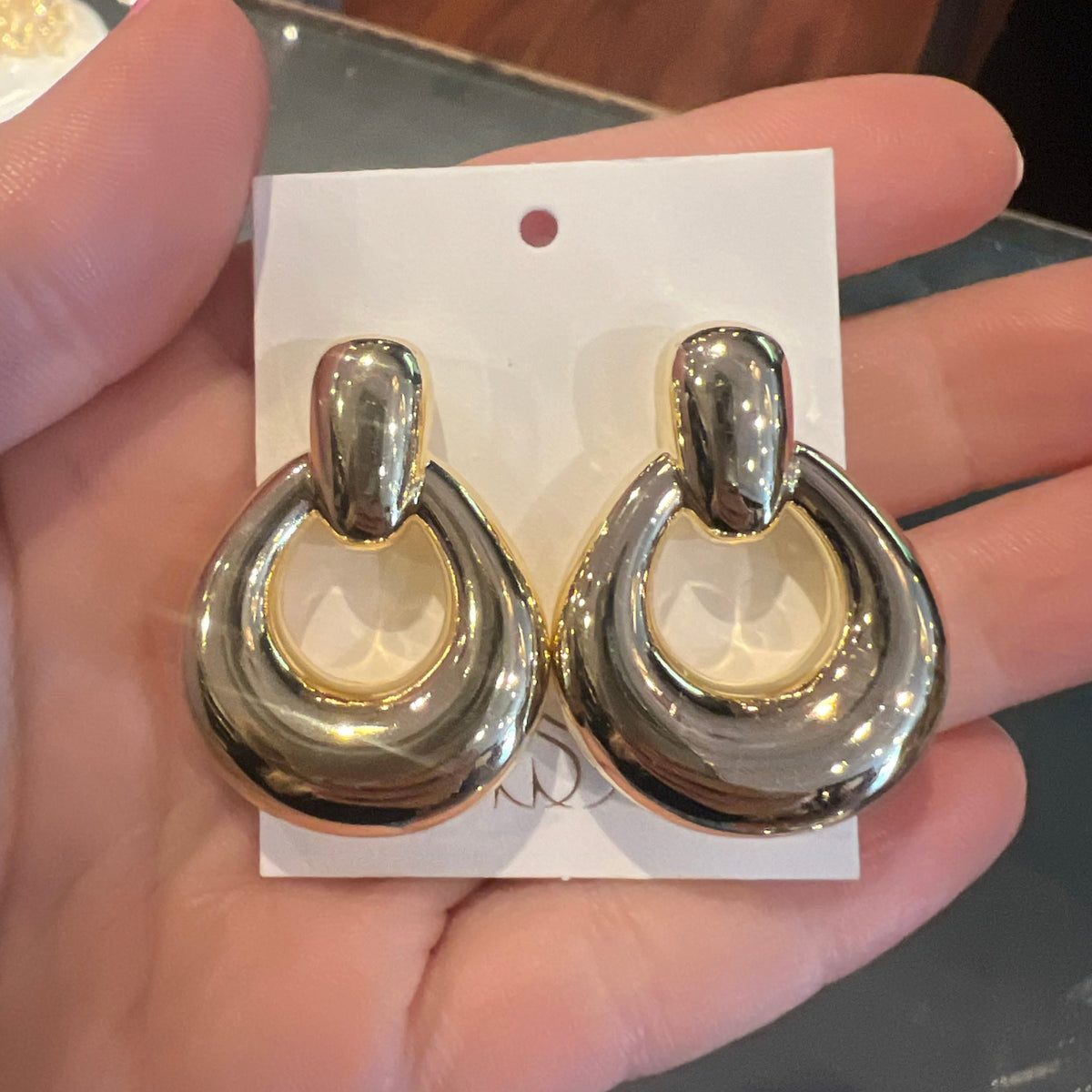 Gold earrings on a white card held by a hand with a blurred background