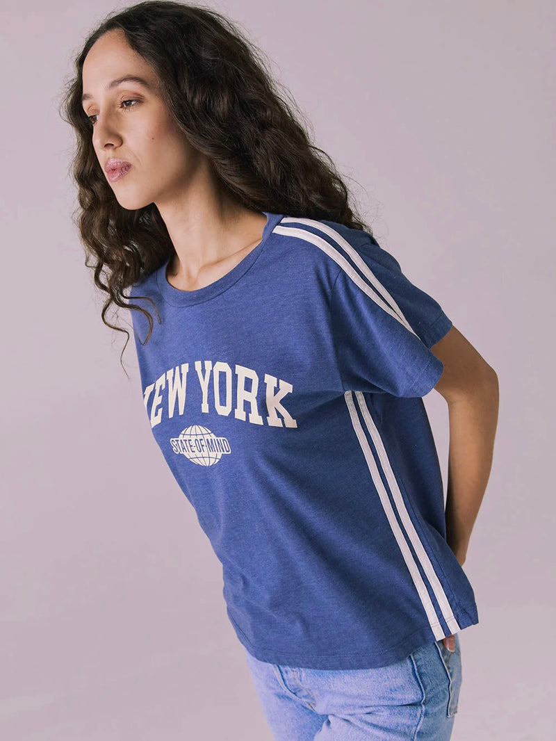 Woman wearing a blue 'New York' t-shirt with white stripes on a plain background