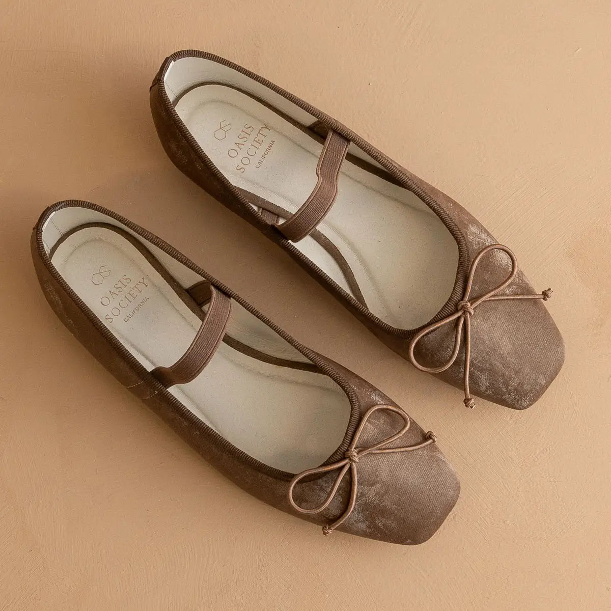 Pair of brown suede shoes with bow detail on a beige background
