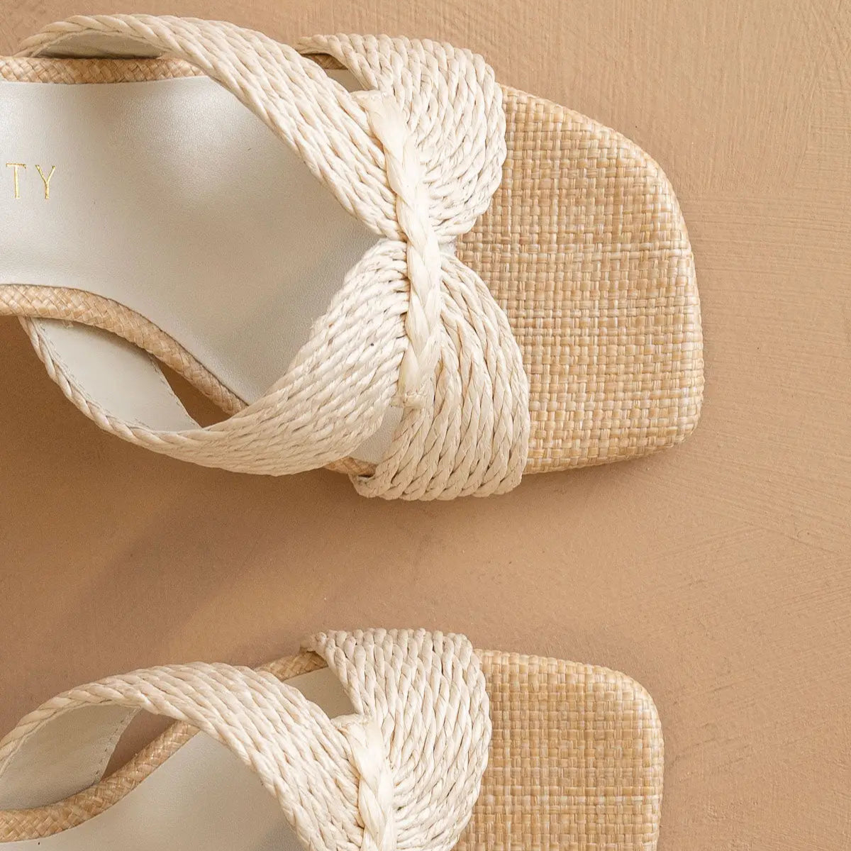 Close-up of woven sandals with white straps on a beige background