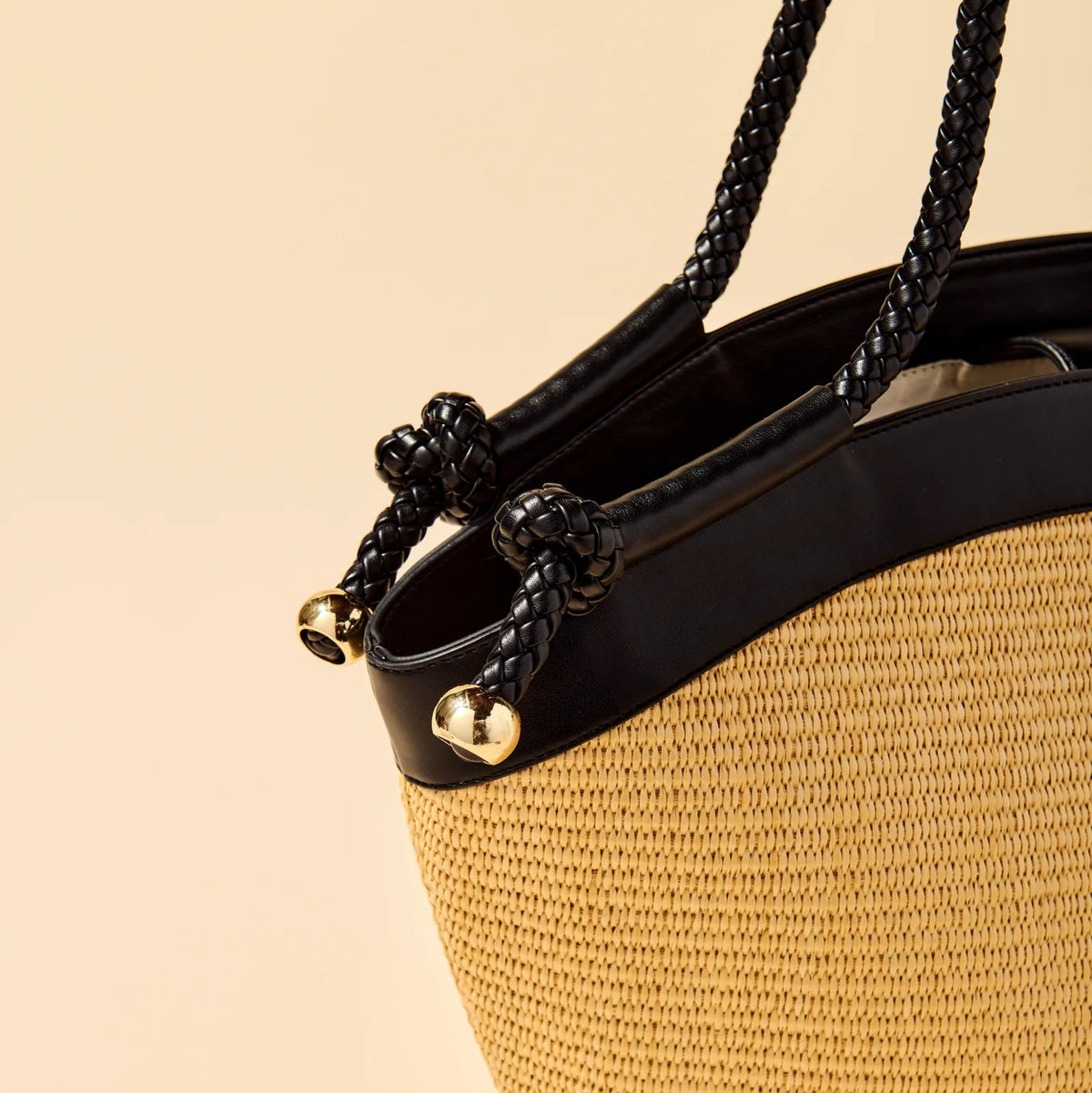 Woven straw handbag with black handle on a beige background