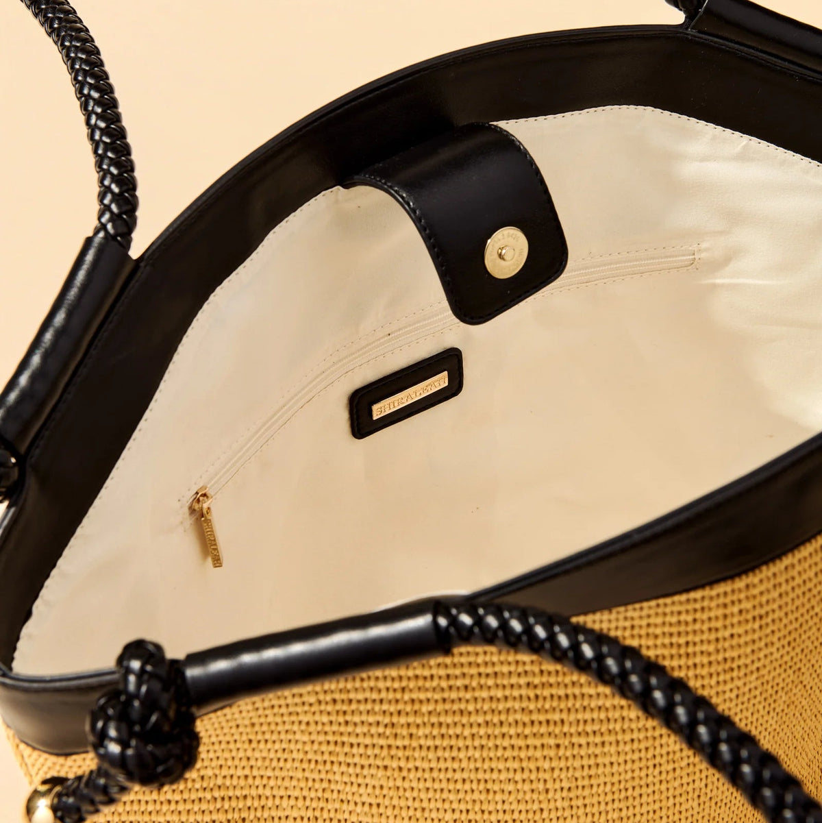 Close-up of a handbag with black handles and gold accents on a beige background