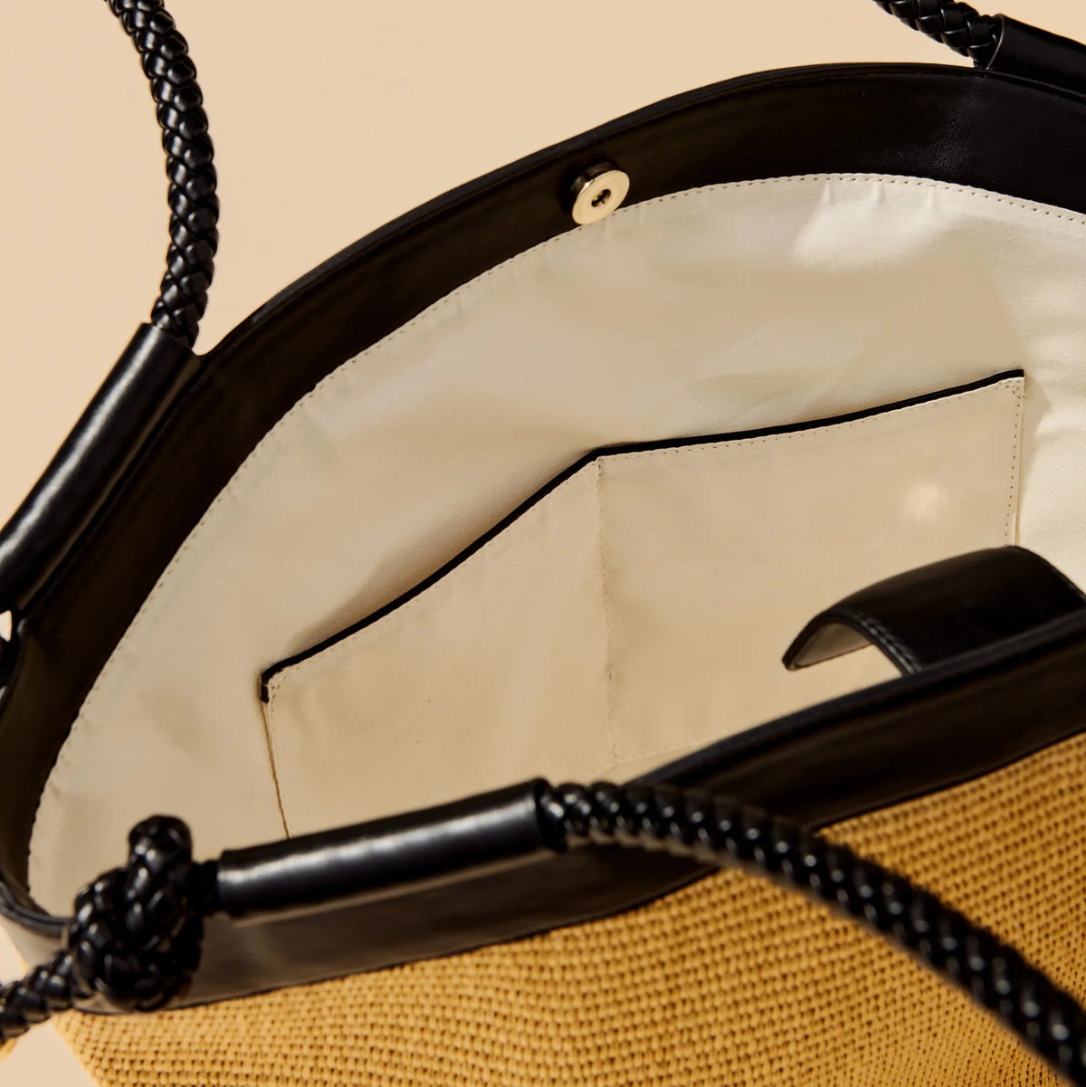 Close-up of a handbag with a black handle and beige interior.