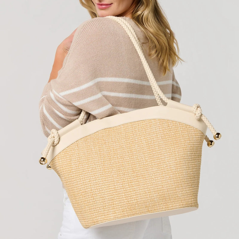 Woman holding a beige woven handbag against a plain background
