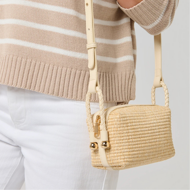 Person wearing a beige and white striped sweater with a beige handbag on a light gray background
