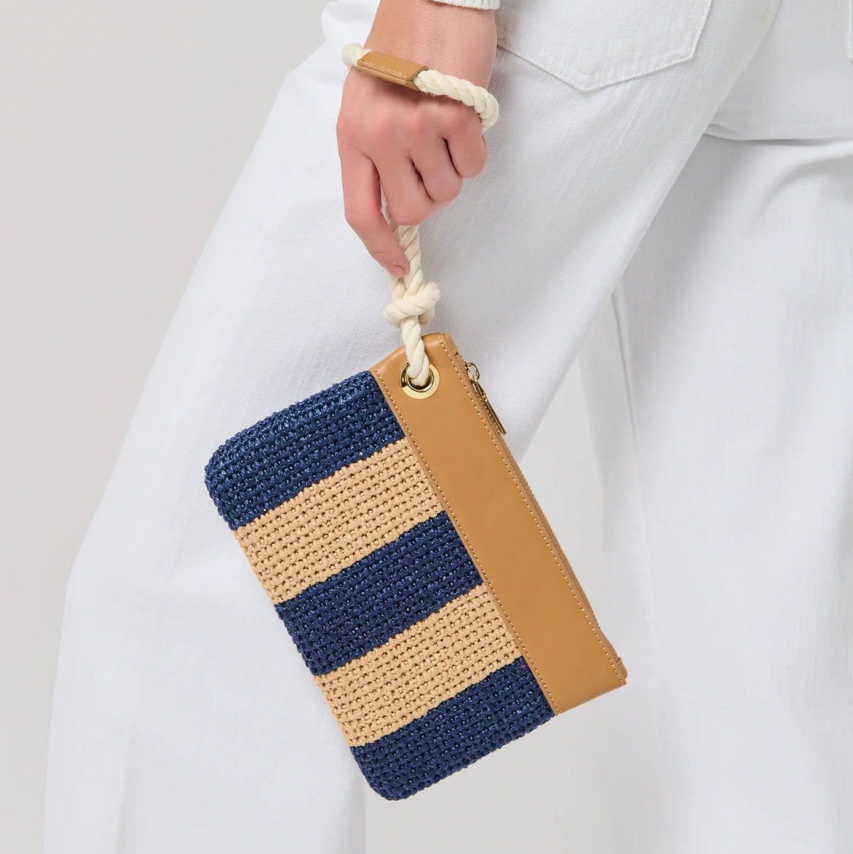 Hand holding a striped clutch bag with blue and brown colors against a plain background
