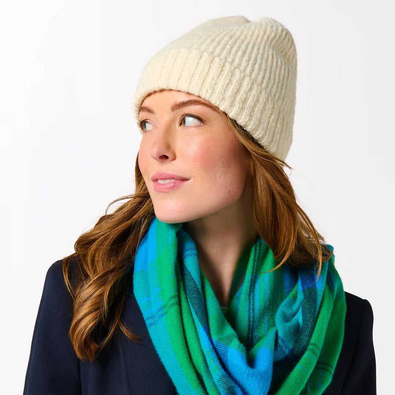 Person wearing a green and blue plaid scarf, navy coat, and cream beanie on a white background