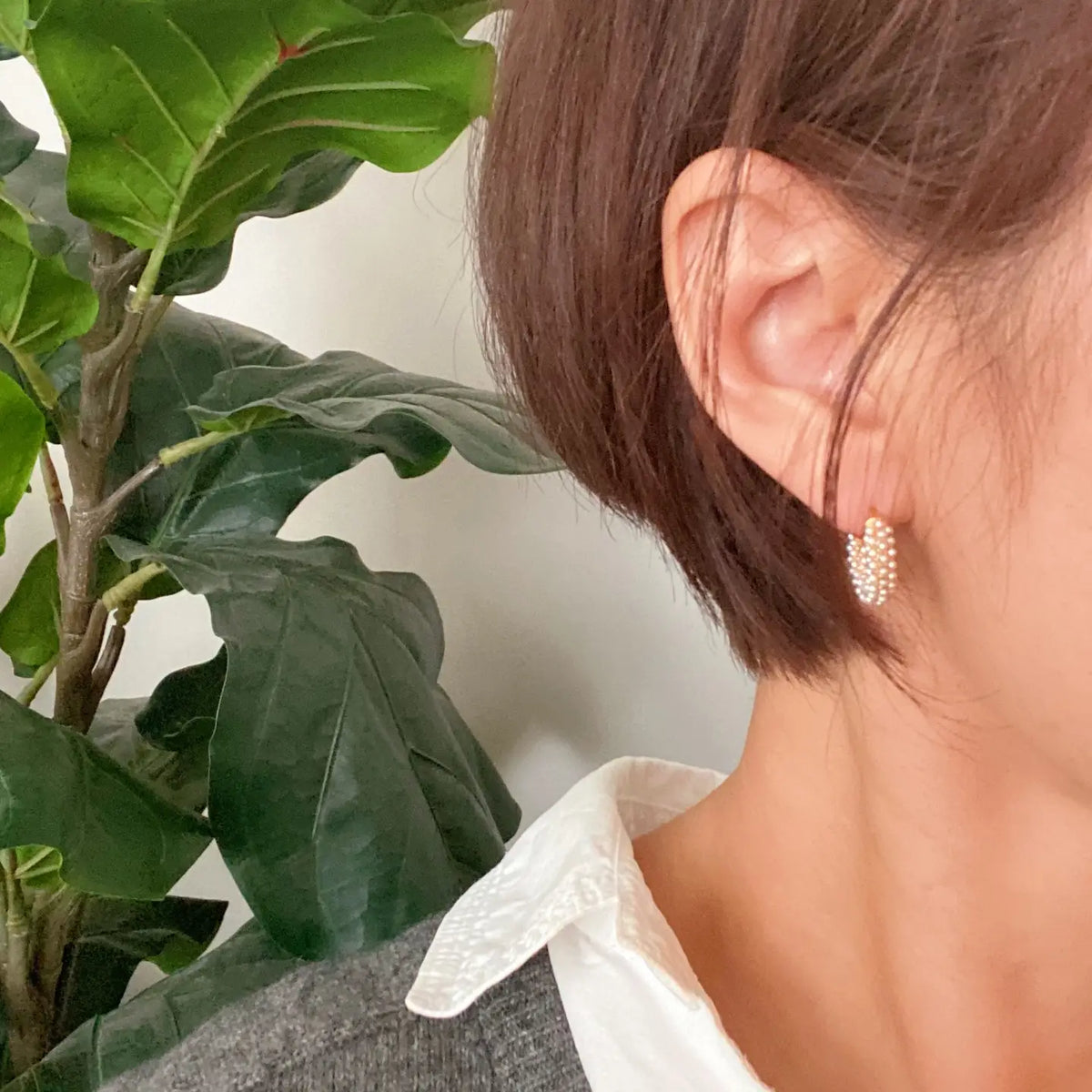 Close-up of a person wearing a gold earring with a plant in the background
