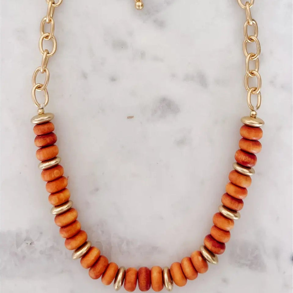 Necklace with orange beads and gold chain on a marble background