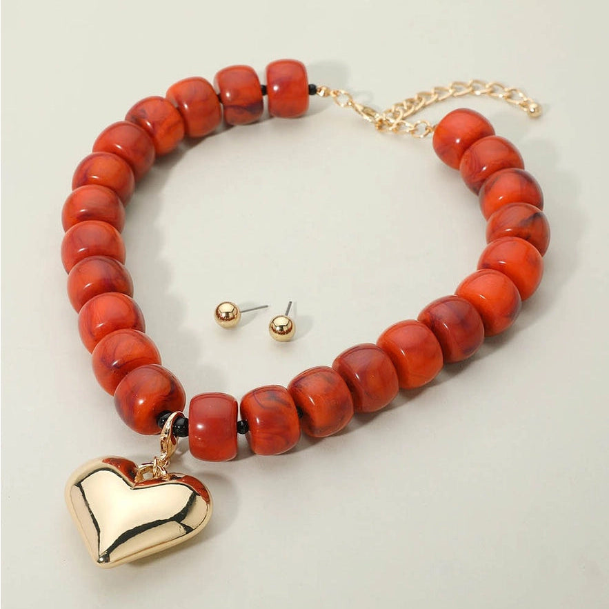 Bracelet with red beads and gold heart charm on a light gray background