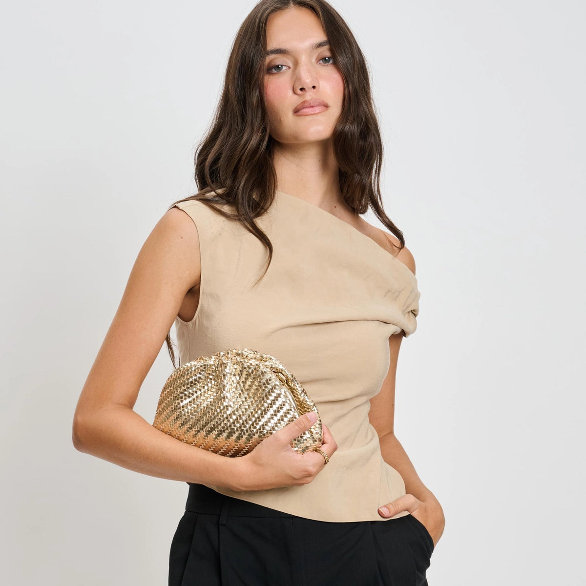 Woman holding a gold clutch against a plain background