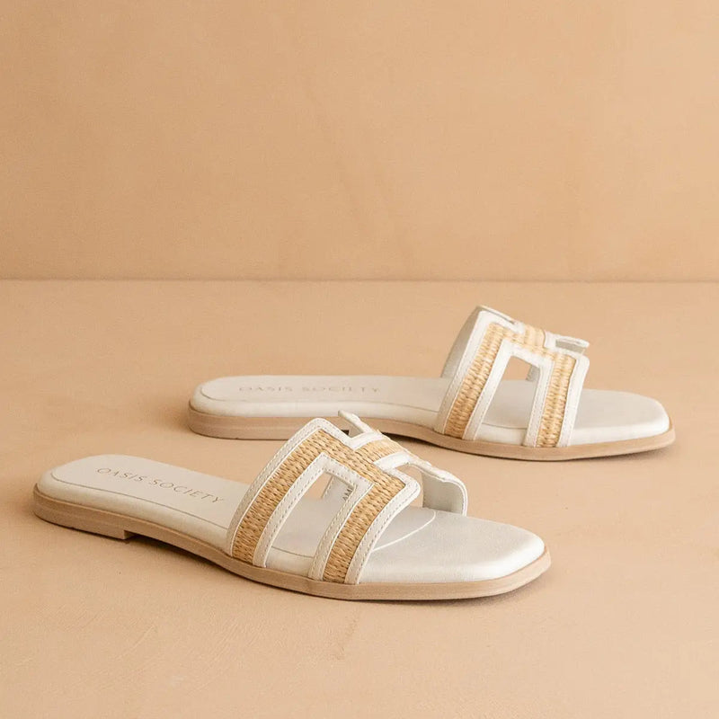 Pair of white sandals with gold straps on a beige background