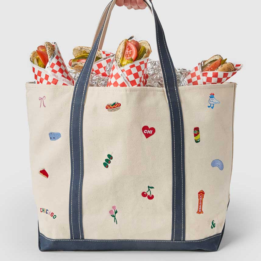 Tote bag with embroidered designs held by a person against a white background