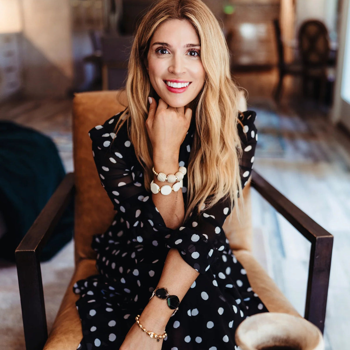 Woman in a black polka dot dress sitting in a chair in a room with a vase on a table.