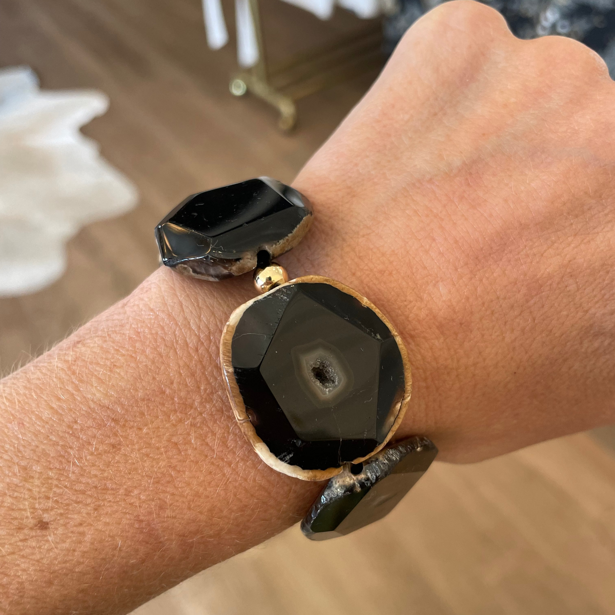 Close-up of a wrist wearing a black and gold bracelet with a blurred indoor background
