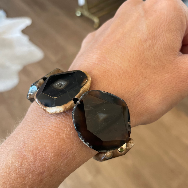 Hand wearing a dark stone-encrusted watch on a blurred indoor background