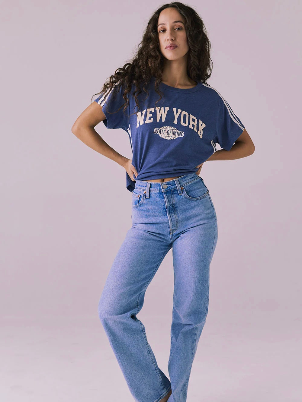 Person wearing a blue 'New York' t-shirt and blue jeans on a plain background