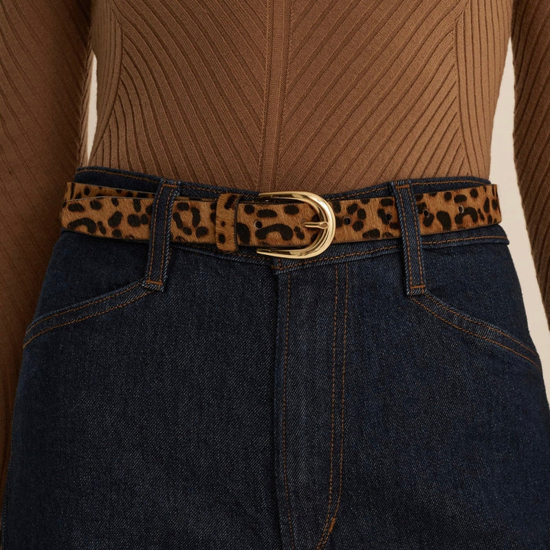A close-up of a leopard print belt with a gold-tone buckle, worn over dark blue jeans and a brown ribbed knit top.