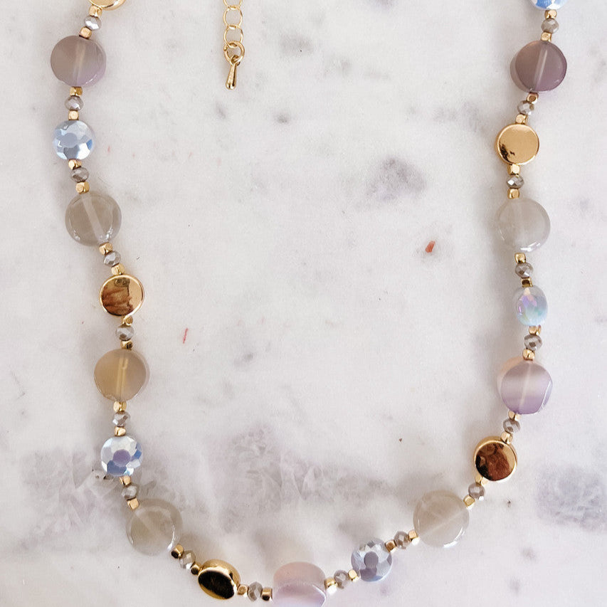 Necklace with multicolored beads on a marble surface with green leaves