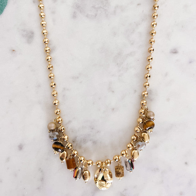 Gold beaded necklace with brown and clear stones on a marble surface