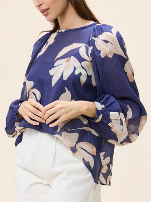 Woman wearing a blue floral blouse and white shorts on a beige background