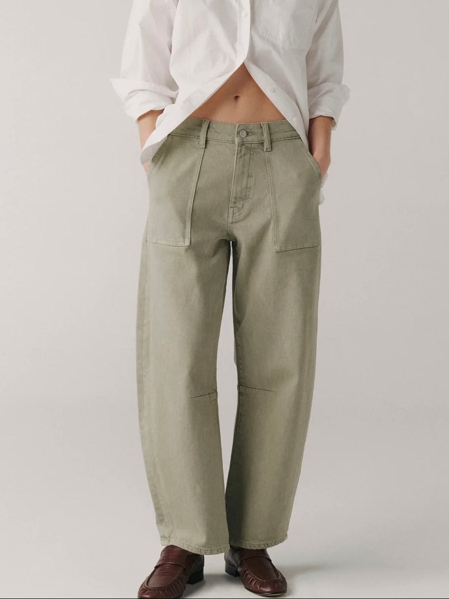 Woman wearing a white shirt and green pants on a plain background