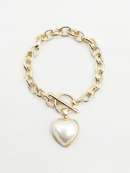Gold chain bracelet with a heart-shaped pearl charm on a white background