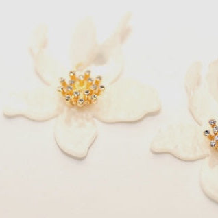 Gold earrings with gemstones on white flowers against a light background