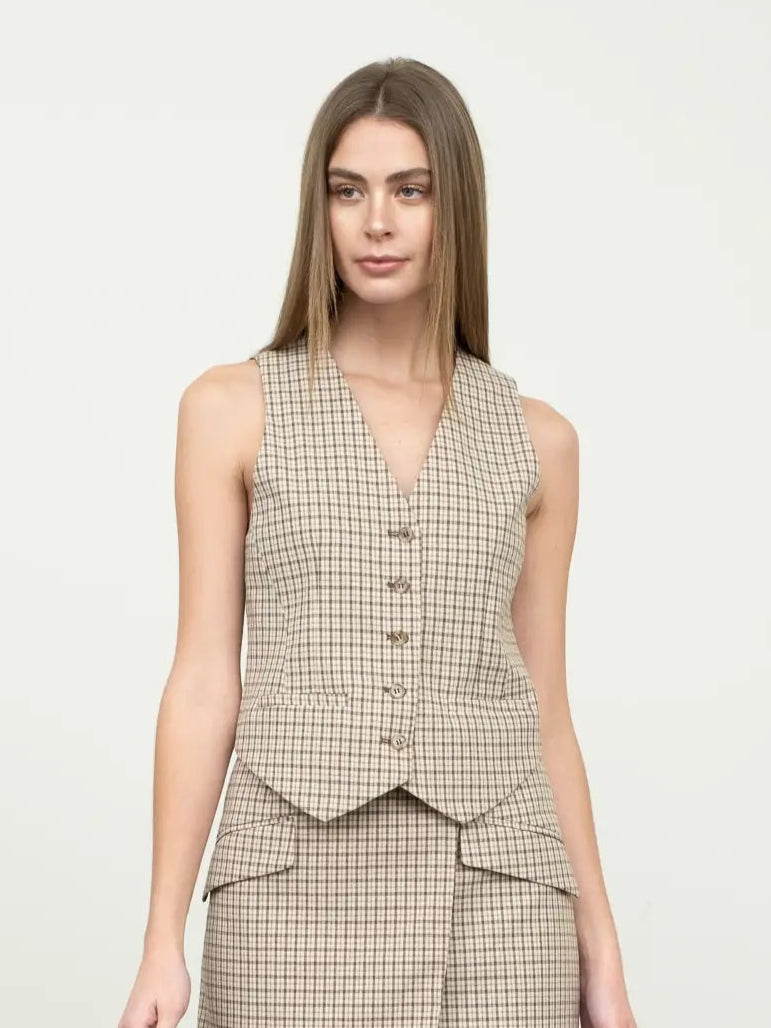Woman wearing a checkered vest and skirt set with brown boots against a white background