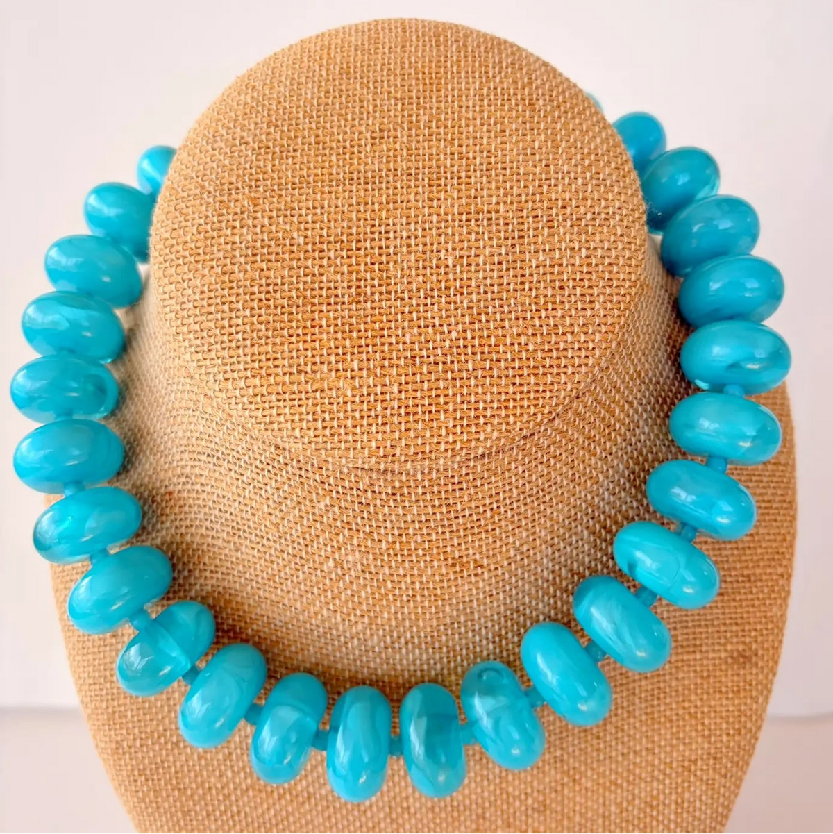 Turquoise necklace on a brown mannequin head against a white background
