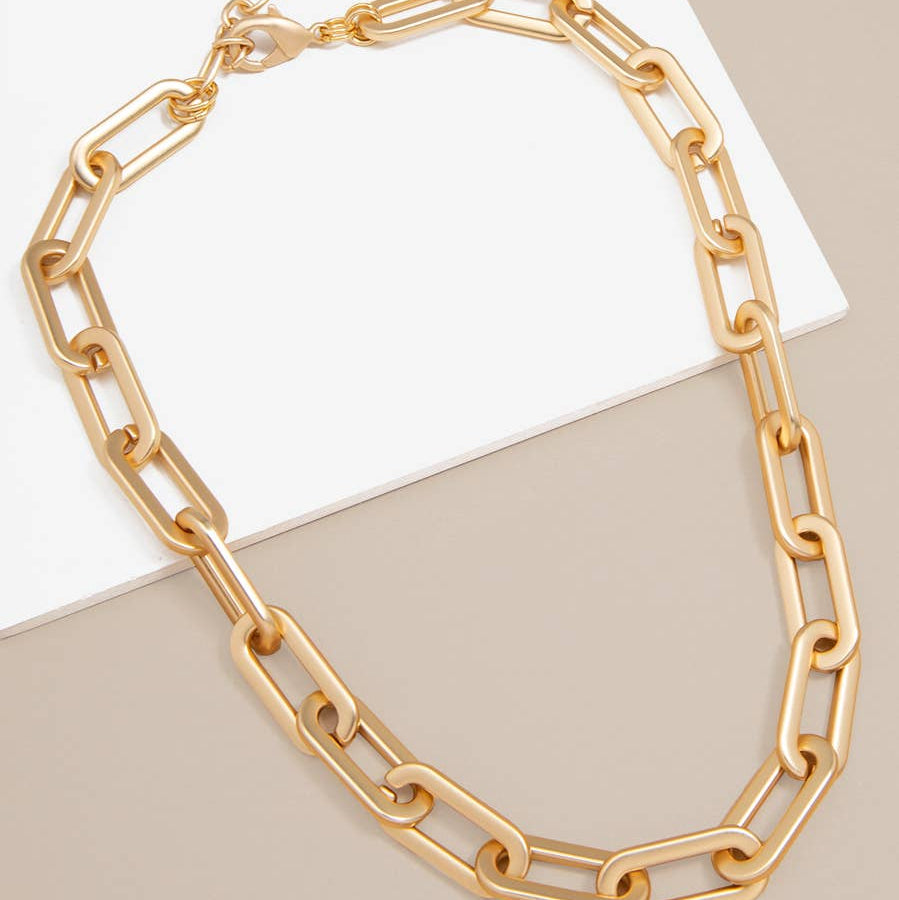 Gold chain necklace on a beige surface with a white card
