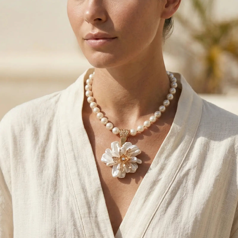 Woman wearing a pearl necklace with a floral pendant against a neutral background