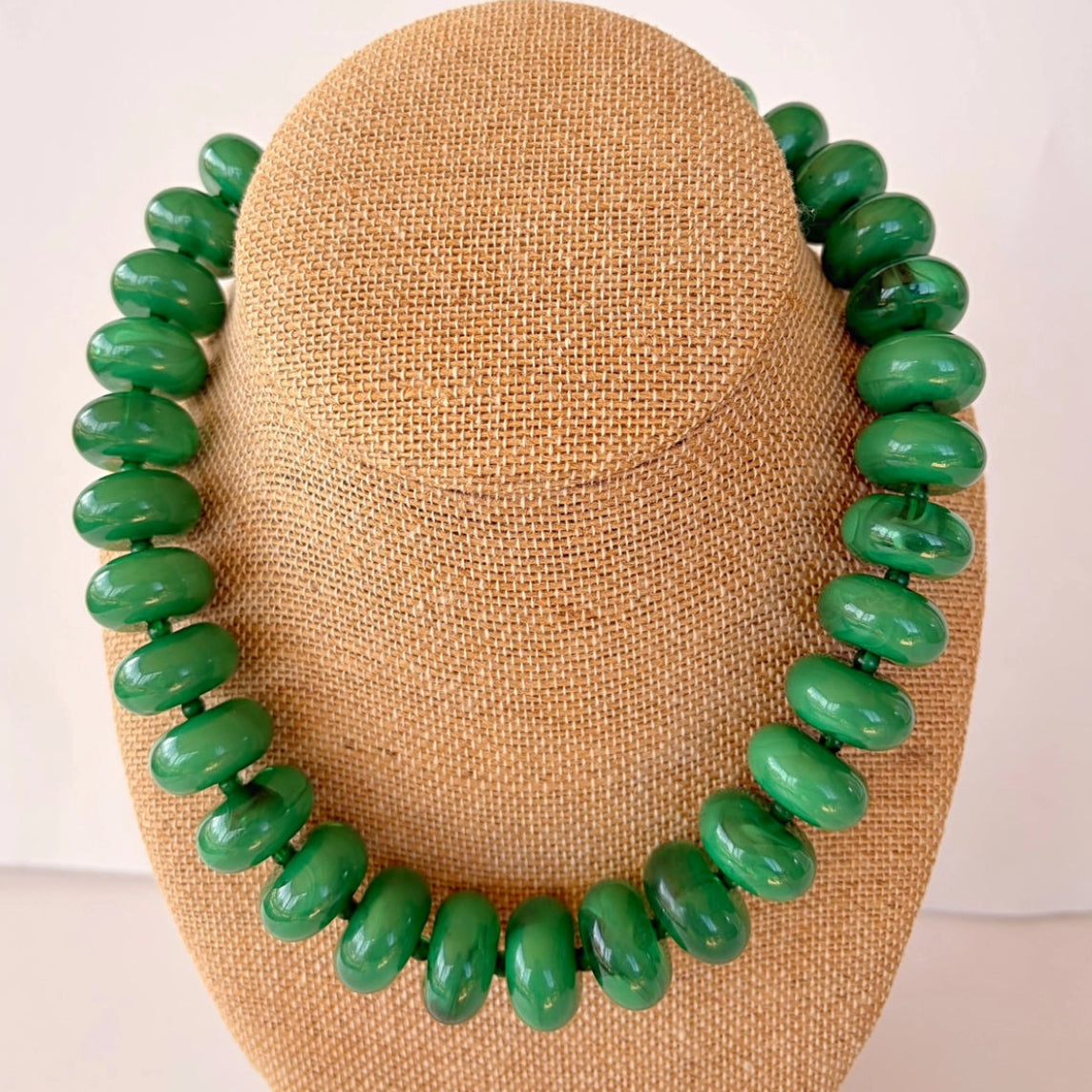 Green beaded necklace on a beige mannequin bust against a white background