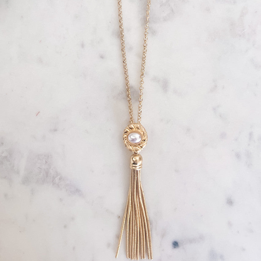 Gold necklace with tassel pendant on a marble surface